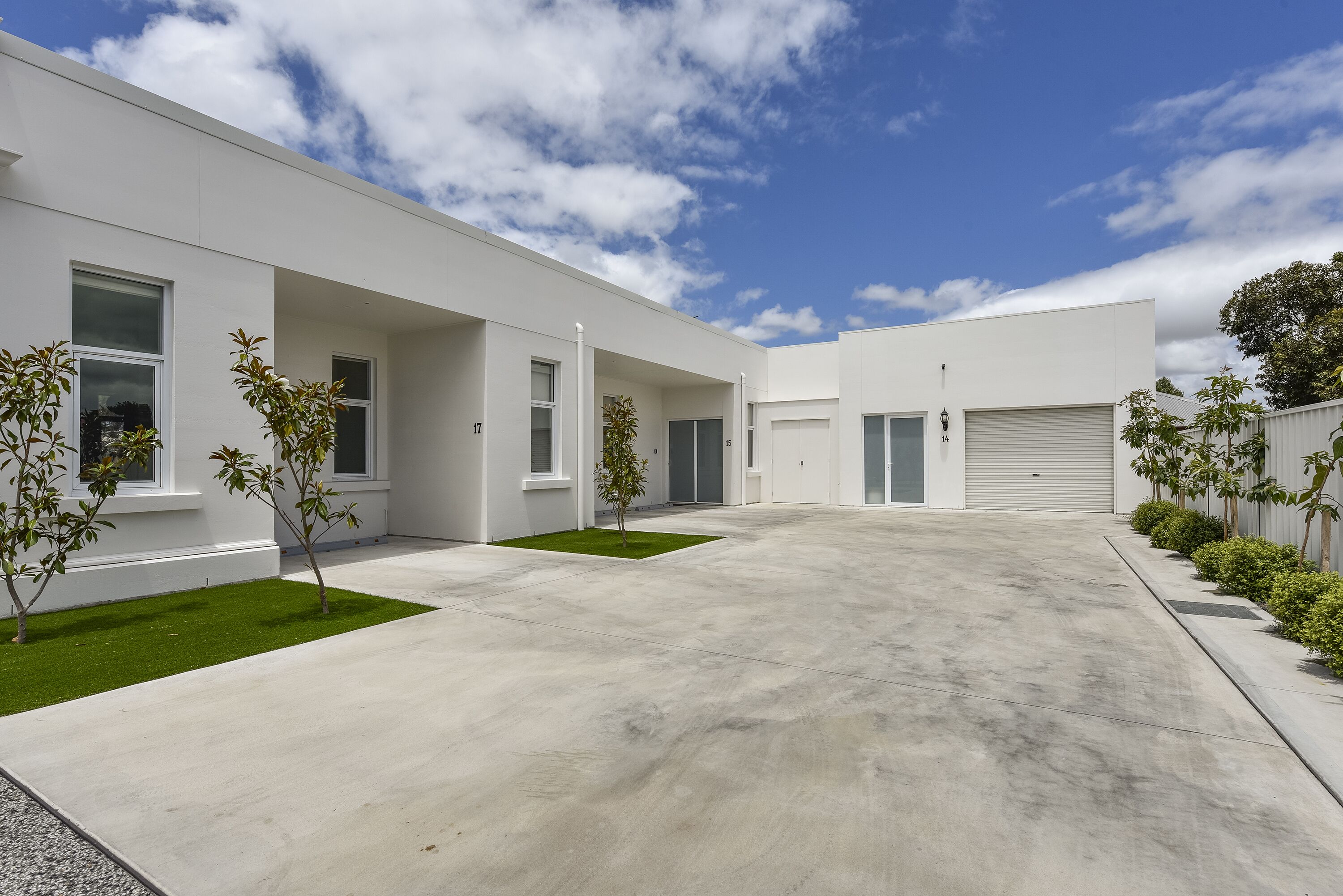A modern building with a flat roof, large windows, and a concrete driveway.