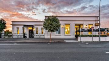 A modern building with a white facade, large windows, and a tree in front.
