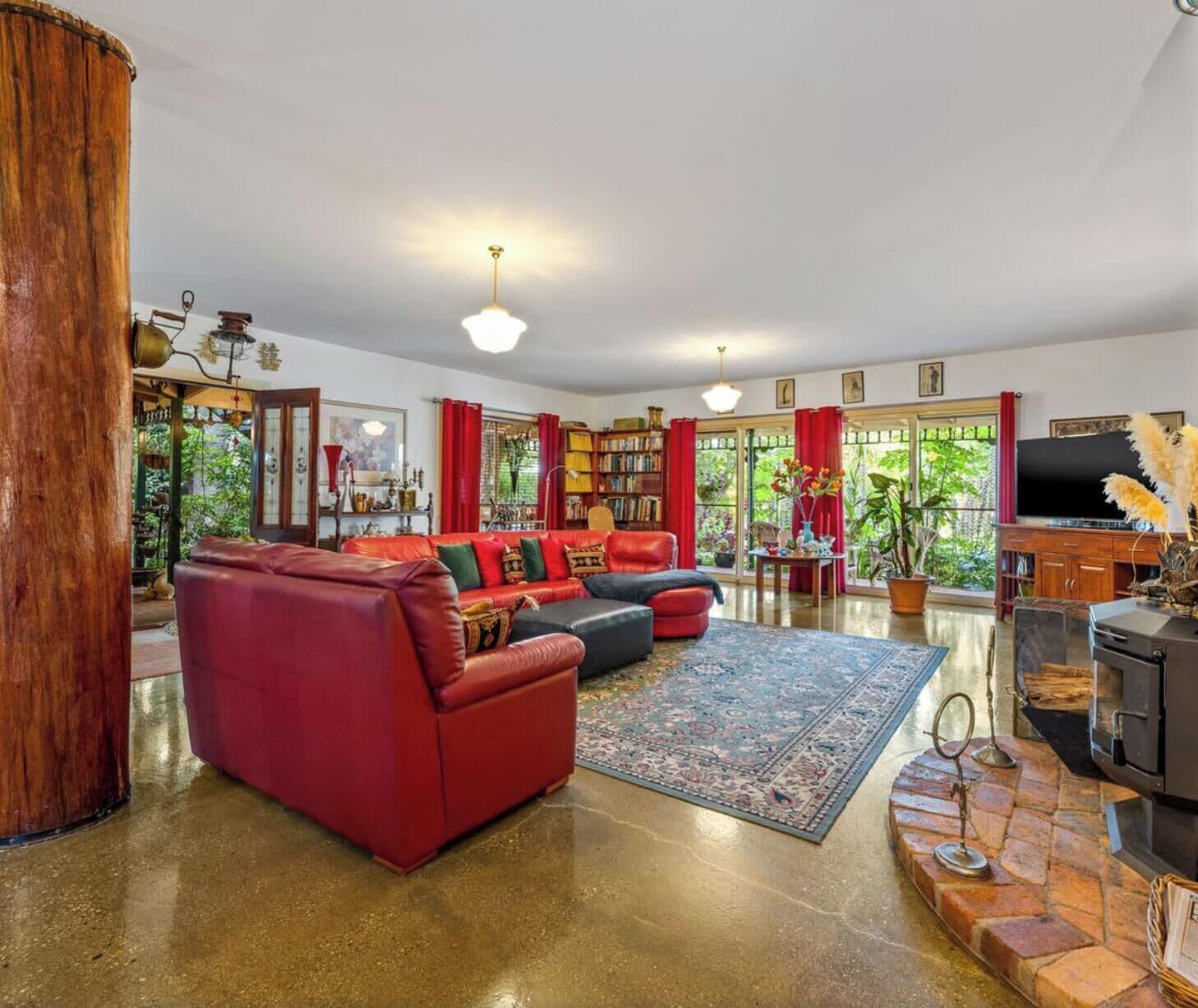 A spacious living room with a red sofa, a fireplace, and a large window with red curtains.
