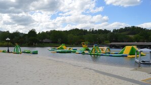 A sandy beach area with water play structures, a clear sky, and a forested hill in the background. - Quaint cabin with a creek in front that will lull you to sleep and pets allowed (Hiawassee)