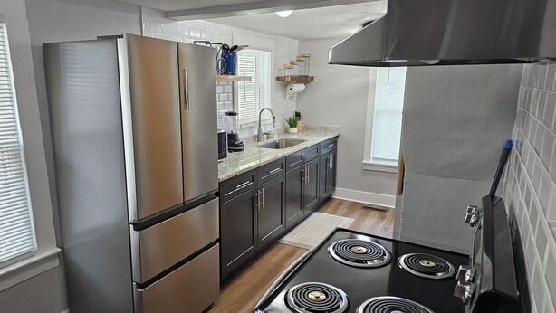 A modern kitchen with stainless steel appliances, dark cabinetry, and a granite countertop. - Cozy Cottage @ Trevecca (Nashville)