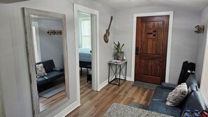 A compact living space with a mirrored wall, a wooden door, a small table with a plant, and a sofa. - Cozy Cottage @ Trevecca (Nashville)