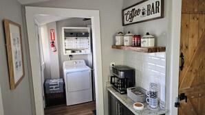 A compact kitchen with a washing machine, a coffee maker, and a coffee bar sign. - Cozy Cottage @ Trevecca (Nashville)