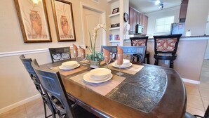 Uma sala de jantar com uma mesa de madeira escura posta para quatro pessoas, rodeada por cadeiras com encostos elaborados.