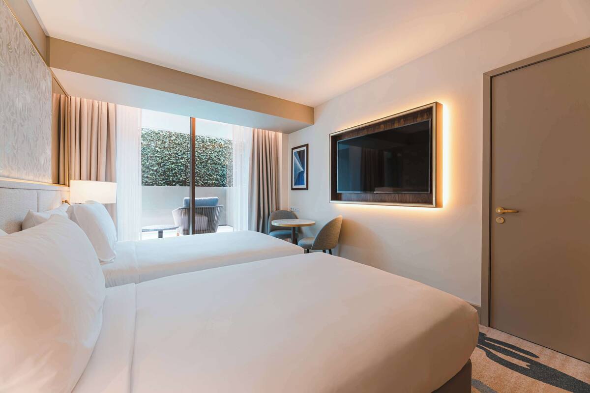 Habitación de hotel con dos camas, un escritorio, una silla, un televisor y una puerta.