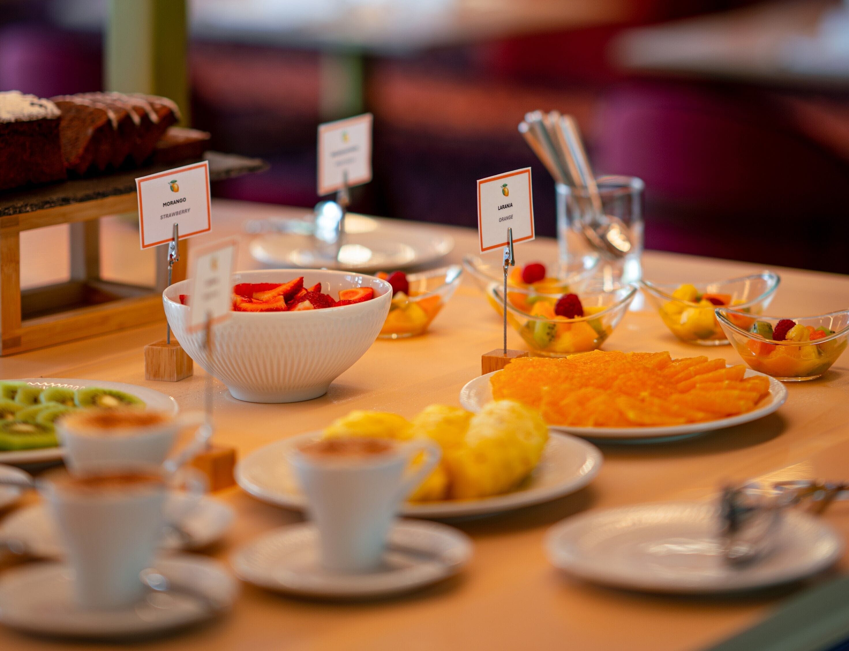 A buffet with various food items including a bowl of strawberries, a plate of orange slices, and a bowl of mixed fruits.