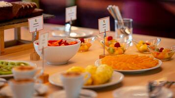 Buffet com diversos alimentos, incluindo uma tigela de morangos, um prato de fatias de laranja e uma tigela de frutas variadas.