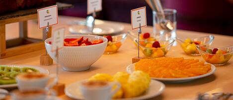 A buffet with various food items including a bowl of strawberries, a plate of orange slices, and a bowl of mixed fruits.