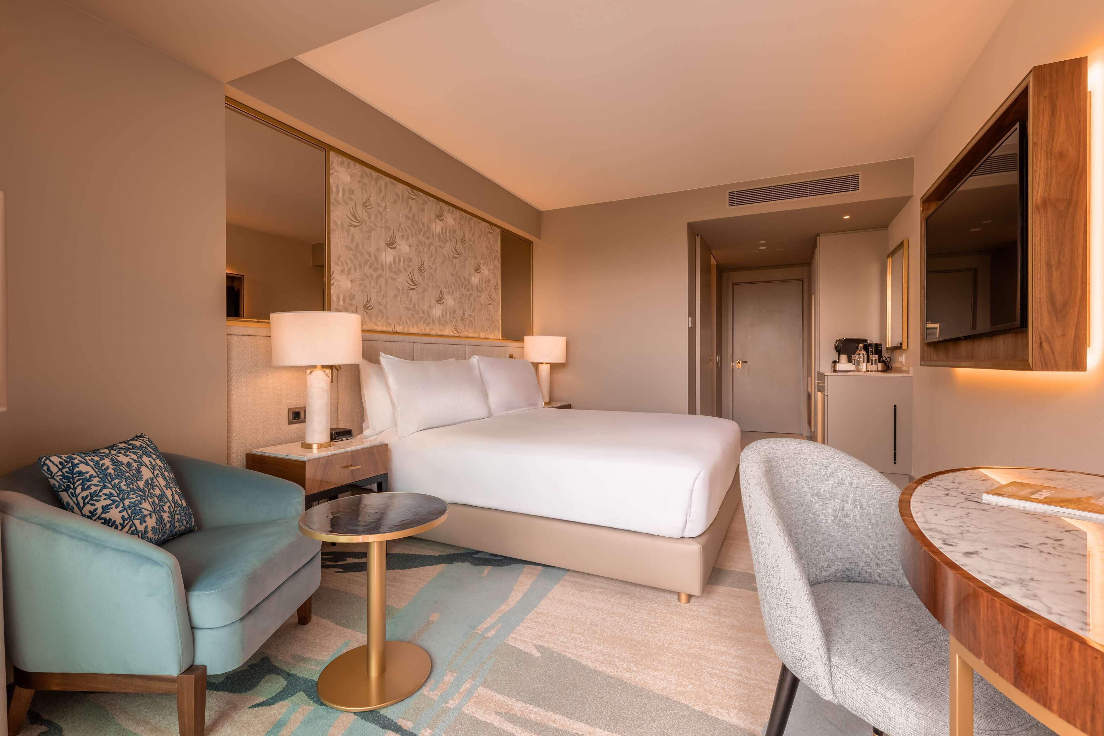 Ein modernes Hotelzimmer mit einem großen Bett, einem kleinen runden Tisch, einer Couch und einem Schreibtisch.