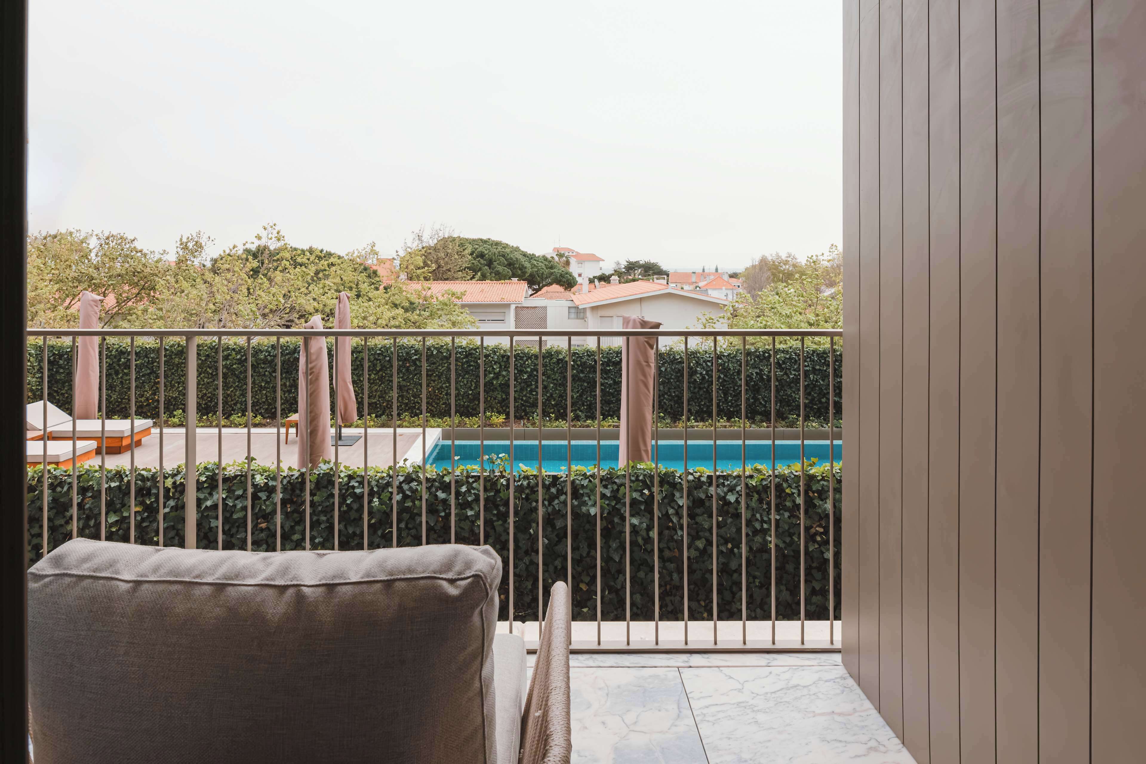 A balcony with a pool, a chair, and a view of houses and trees.