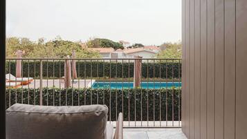 A balcony with a pool, a chair, and a view of houses and trees.