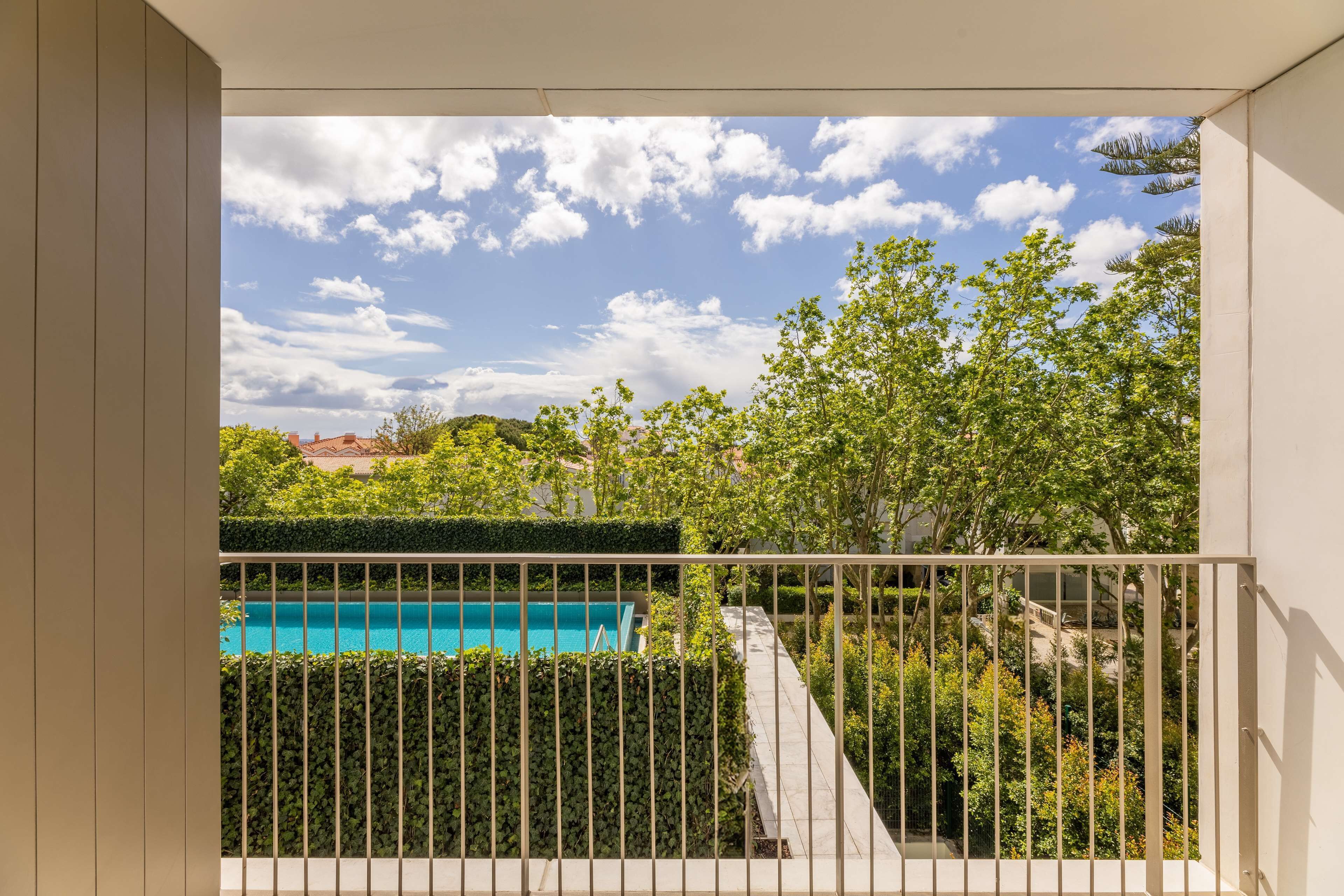 A balcony with a view of a swimming pool, surrounded by greenery and trees.
