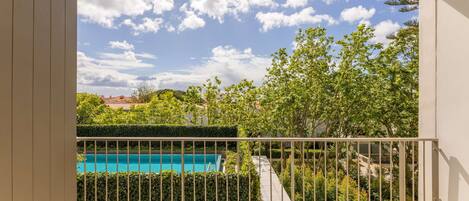 A balcony with a view of a swimming pool, surrounded by greenery and trees.