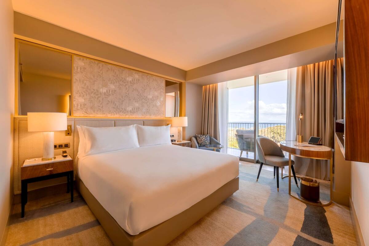 Habitación de hotel con una cama grande, un escritorio con una computadora portátil, una silla y vistas al exterior.