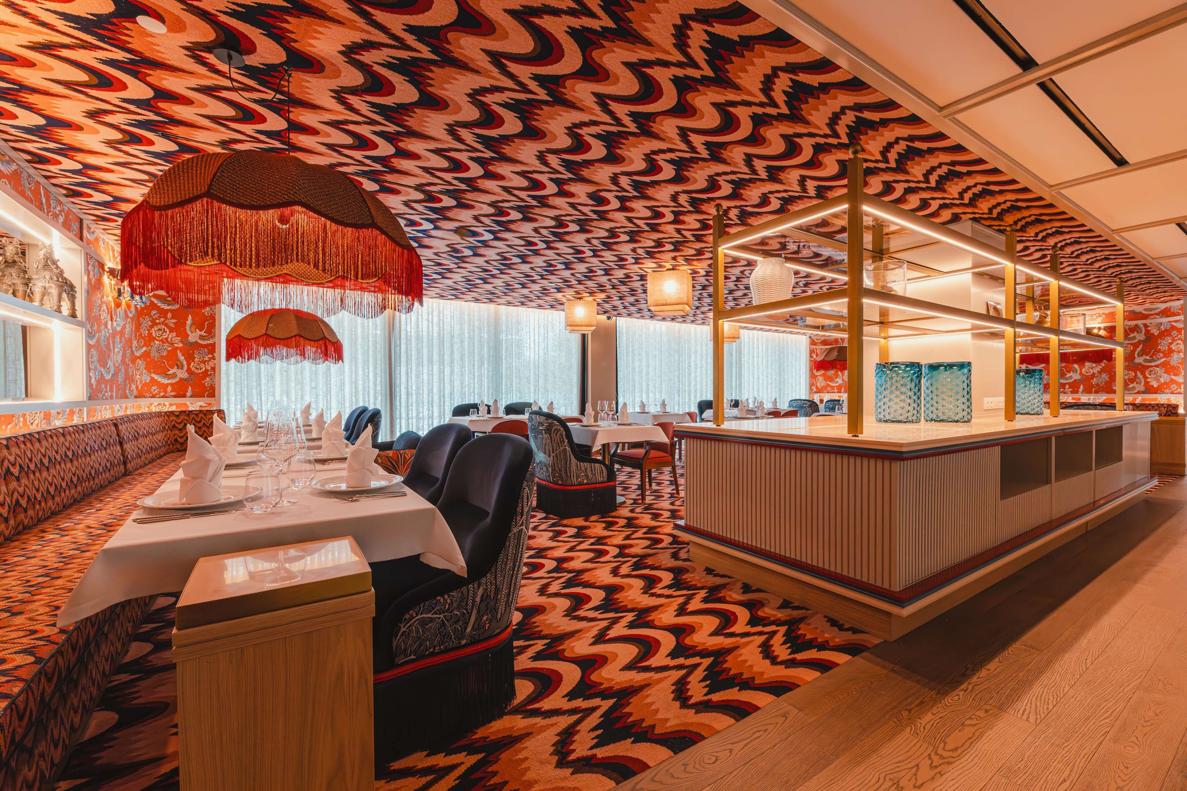 A restaurant with a patterned ceiling, wooden paneling, and a central bar area.