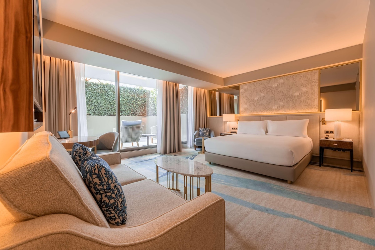 Habitación de hotel con una cama grande, un sofá, una mesita y vistas al exterior.