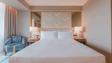 A hotel room with a large bed, two bedside tables with lamps, a chair, and a large mirror above the bed.