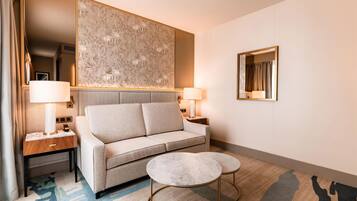 Una habitación de hotel moderna con un sofá, dos mesas redondas, un panel decorativo y un espejo.