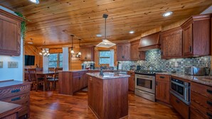 A spacious kitchen with wooden cabinetry, a central island, and a tiled backsplash. - Chateau Laurel in Lake Lure | Private 5,000 Sq Ft Cabin in Blue Ridge Mountains! (Lake Lure)
