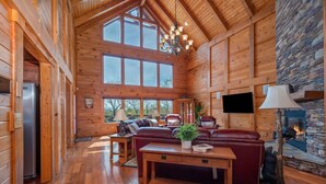 A log cabin interior with a stone fireplace, wooden furniture, and a large window. - Chateau Laurel in Lake Lure | Private 5,000 Sq Ft Cabin in Blue Ridge Mountains! (Lake Lure)