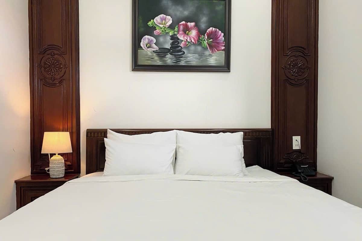 Ein Hotelzimmer mit einem großen Bett, zwei Nachttischen, einer Lampe und einem Blumenbild an der Wand.