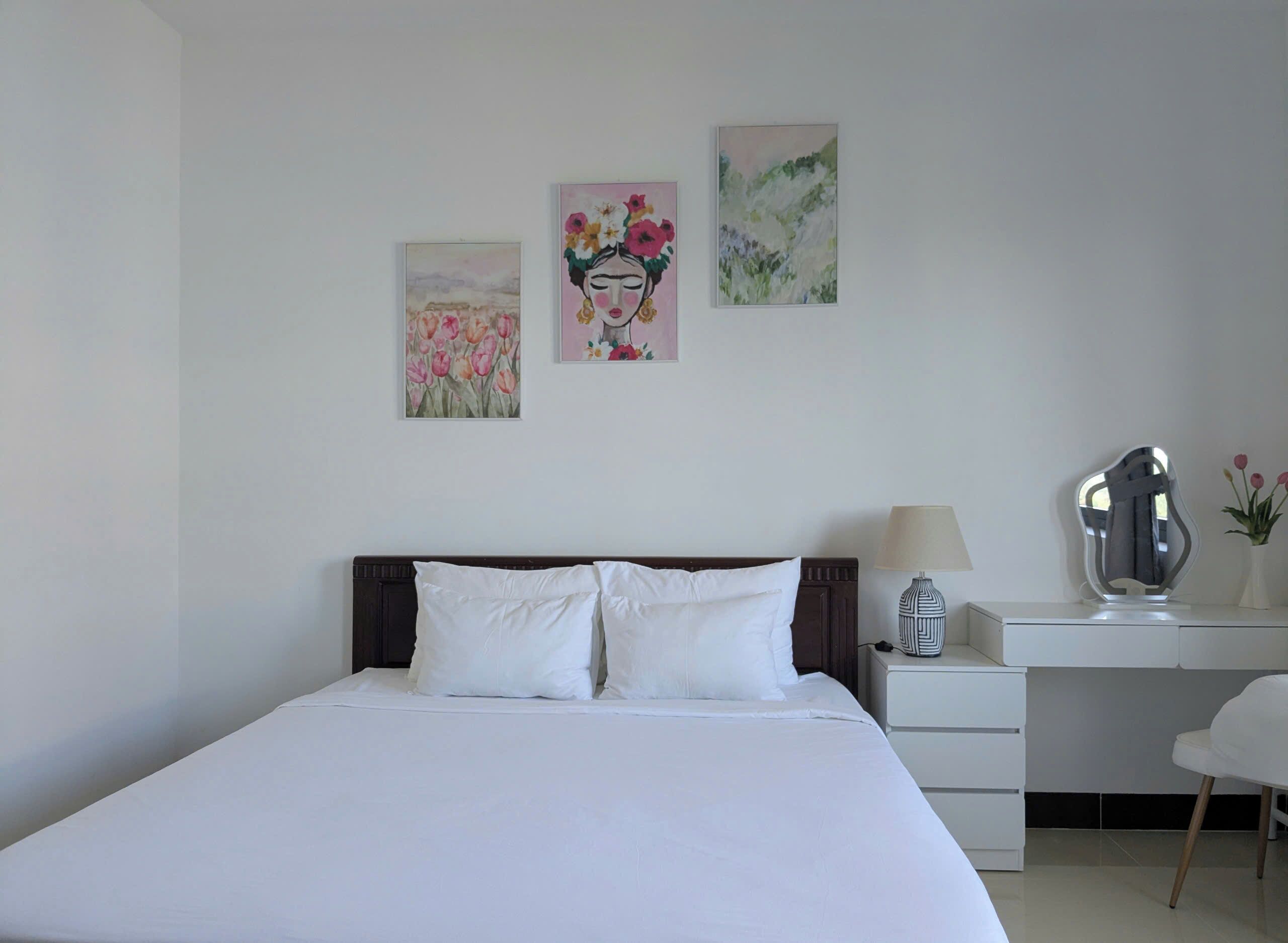 Quarto bem arrumado com uma cama grande, uma escrivaninha e uma cadeira. Há três obras de arte na parede.