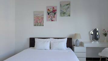 Quarto bem arrumado com uma cama grande, uma escrivaninha e uma cadeira. Há três obras de arte na parede.