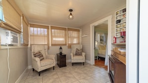 A cozy room with two armchairs, a small table, and a lamp. There are large windows with blinds, a ceiling light, and a shelf with various items. - Best Location downtown GJ - Beautifully updated 2 Bedroom! (Grand Junction)