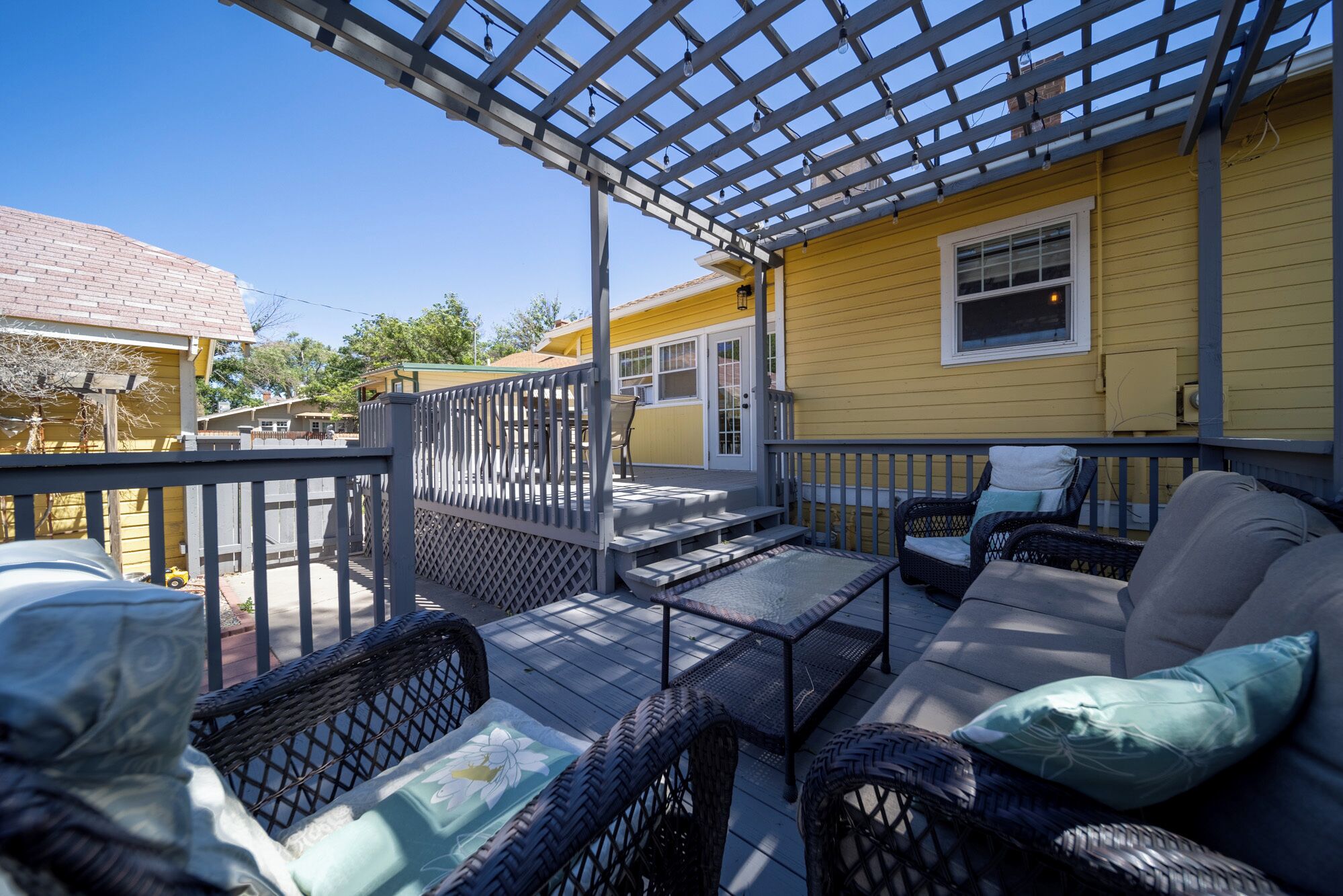 Une terrasse extérieure couverte, aménagée avec des meubles en osier et surmontée d’une pergola.