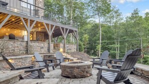A stone patio with Adirondack chairs and a stone fire pit. - *Luxury* Home, Ski in/out, Hot Tub, Firepit, Games & More! (Beech Mountain)