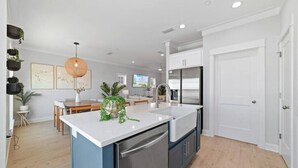 A modern kitchen with a central island, built-in appliances, and a dining area in the background. - Summer Vacation! Beach, Pool, Games, Sleeps 10! (Orange Beach)