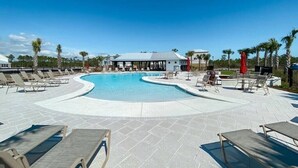 A pool area with lounge chairs and a building in the background. - Summer Vacation! Beach, Pool, Games, Sleeps 10! (Orange Beach)
