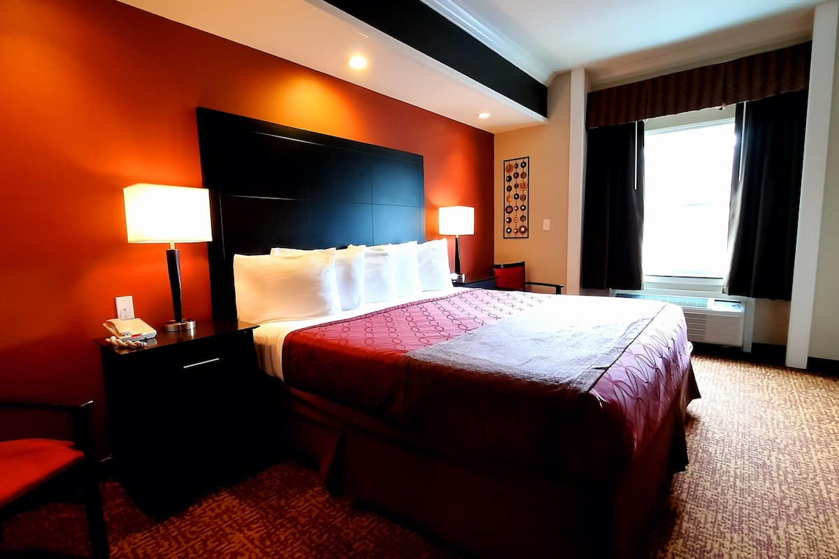 A hotel room with a large bed, two bedside lamps, a desk with a telephone, a chair, and a window with curtains.