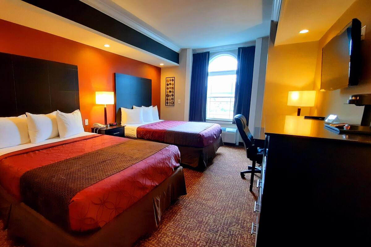 A hotel room with two beds, a desk, a chair, and a TV.