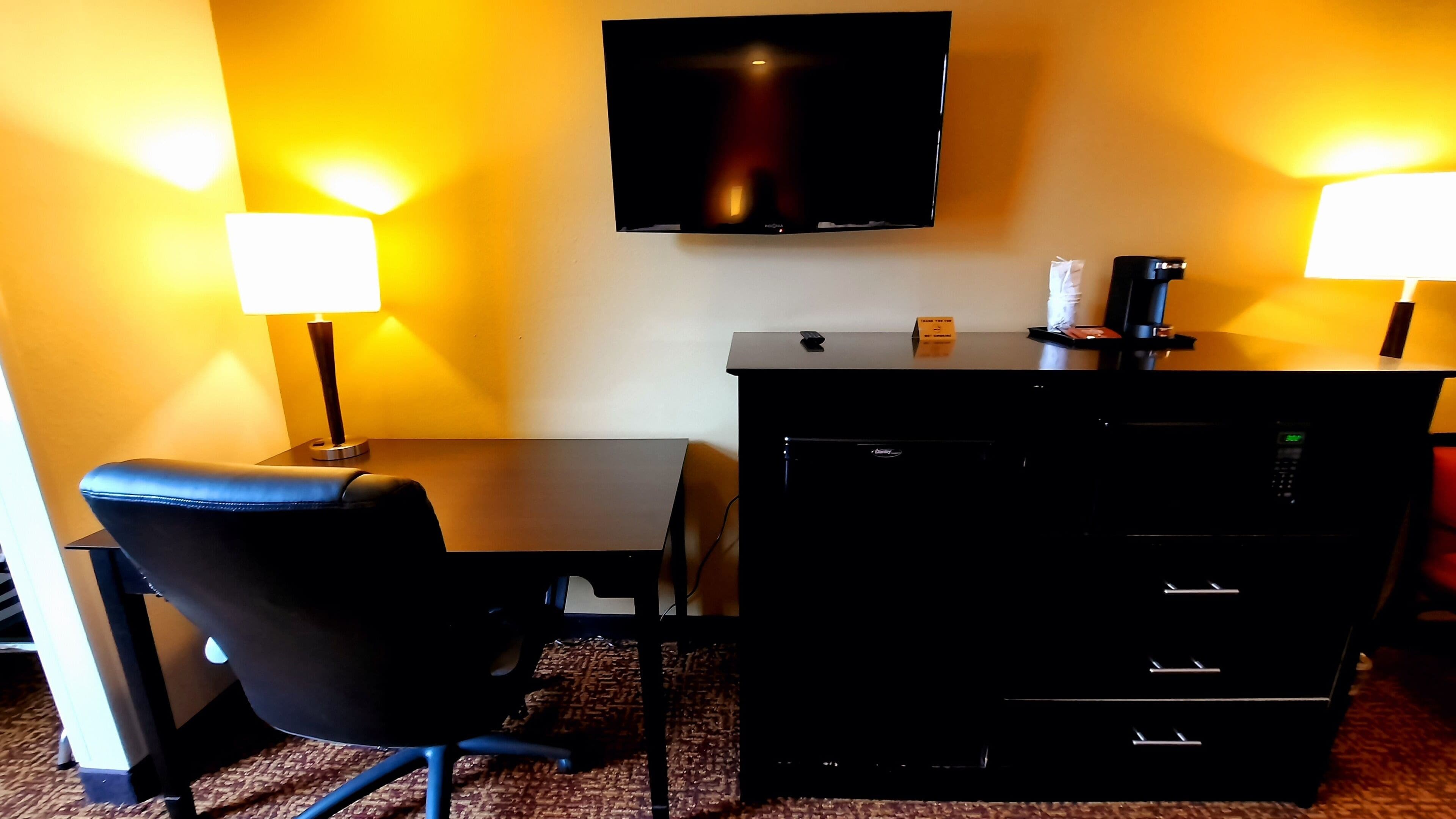 A hotel room with a desk, chair, flat-screen TV, two bedside lamps, and a minibar.