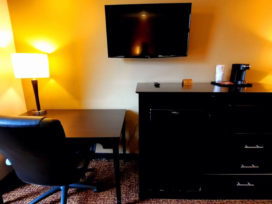 A hotel room with a desk, chair, flat-screen TV, two bedside lamps, and a minibar.