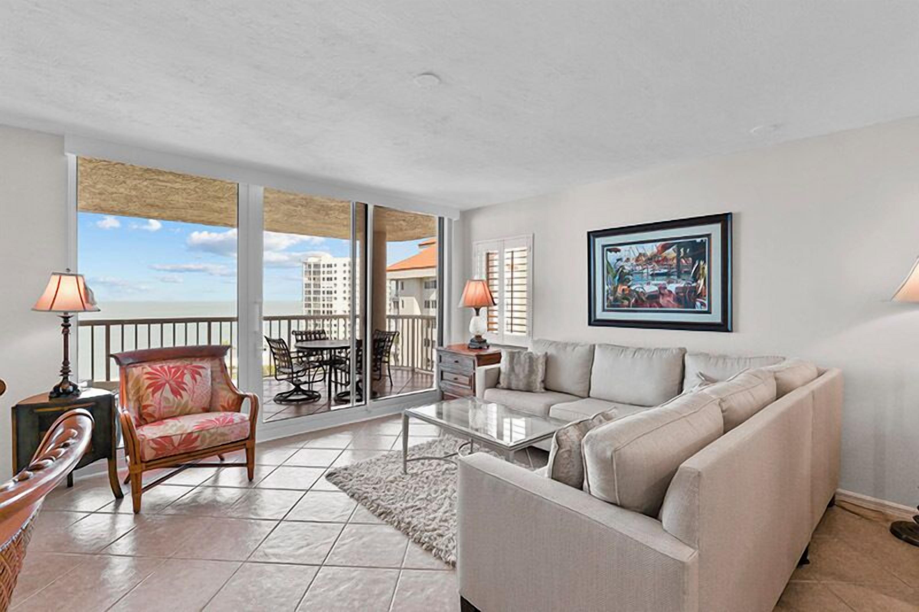 A spacious living room with a large window, a sofa, a chair, and a dining table.