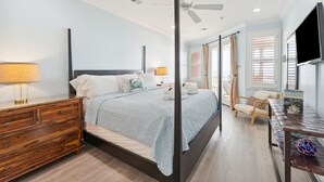 Ein Schlafzimmer mit Bett, Holzkommode, Deckenventilator und Fernseher.
