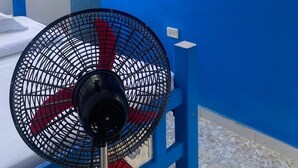 A room with a bed, a standing fan, a window with metal bars, and a blue wall. - APARTMENT WITH BALCONY ECONOMIC, QUIET, IN COUNTRY HOUSE NEAR THE SEA (SANTA MARTA)