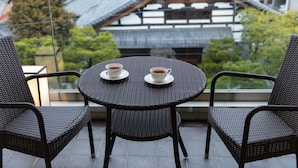 A balcony with wicker chairs and a table, two cups of tea, and a traditional Japanese building in the background. - Rinn Gion Hanatouro (Kyoto)