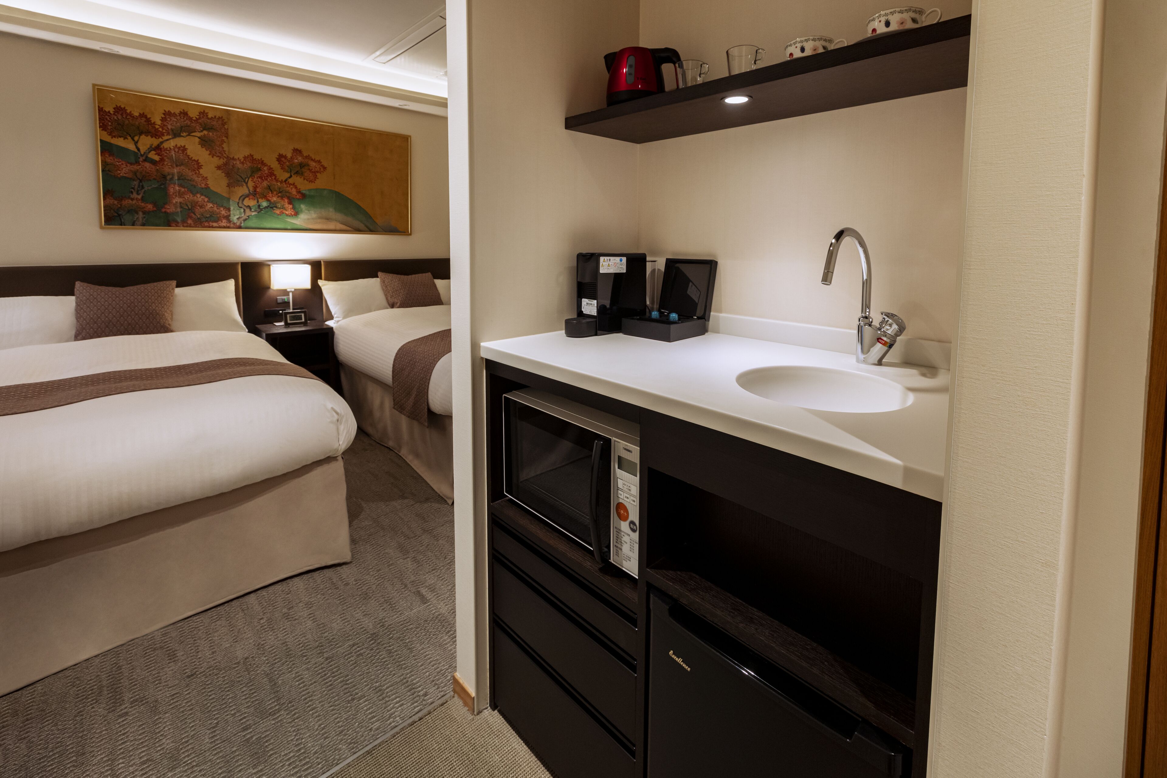 A hotel room with a bed, bedside table, lamp, microwave, coffee maker, and a sink.