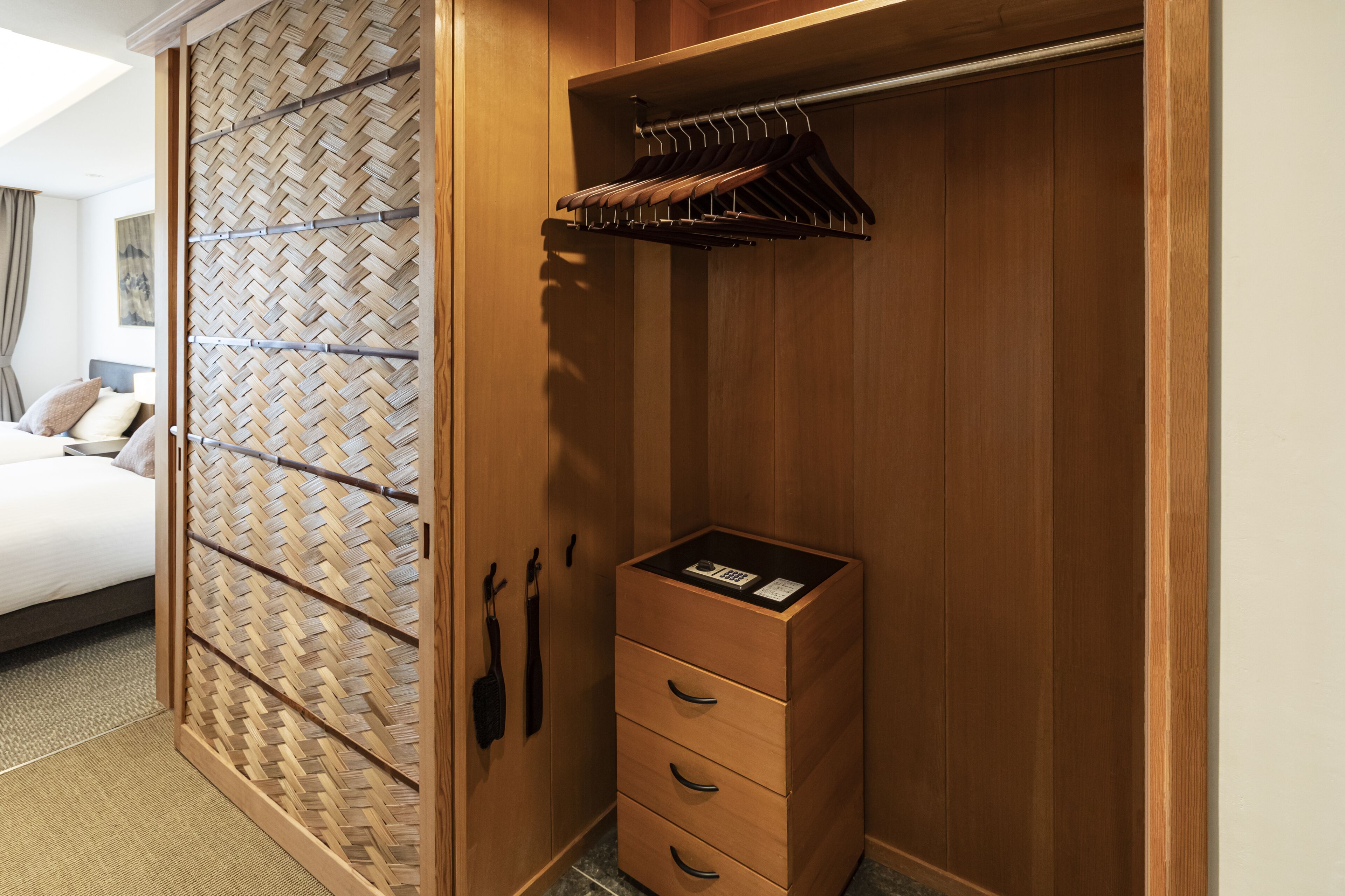 A wooden wardrobe with a herringbone-patterned sliding door, a hanging rack, and a small drawer unit.