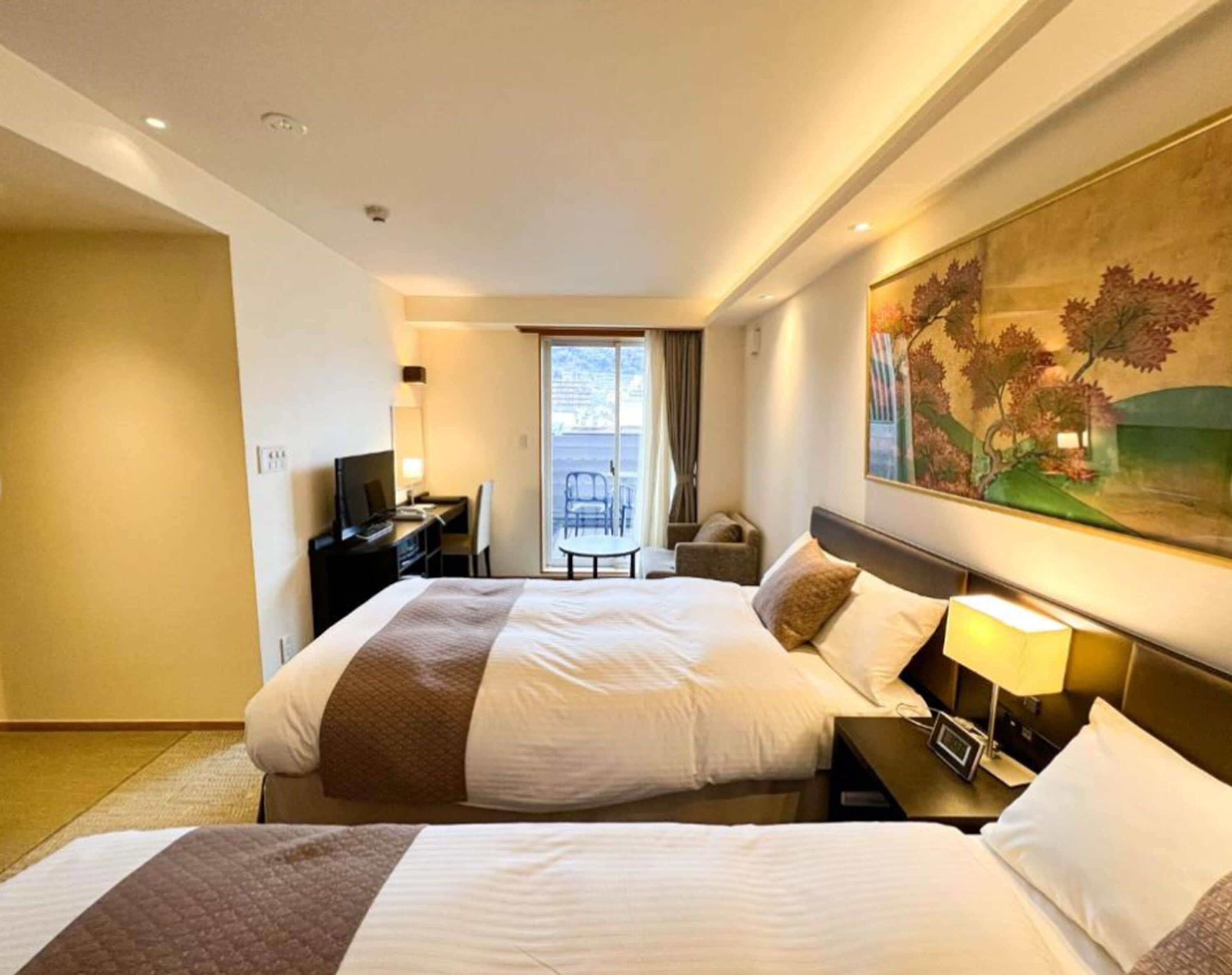 A hotel room with two beds, a desk, a chair, a TV, and a painting on the wall.