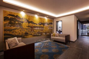A modern lobby with a large traditional mural, a glass coffee table, and a sofa with a patterned rug. - Rinn Gion Hanatouro (Kyoto)
