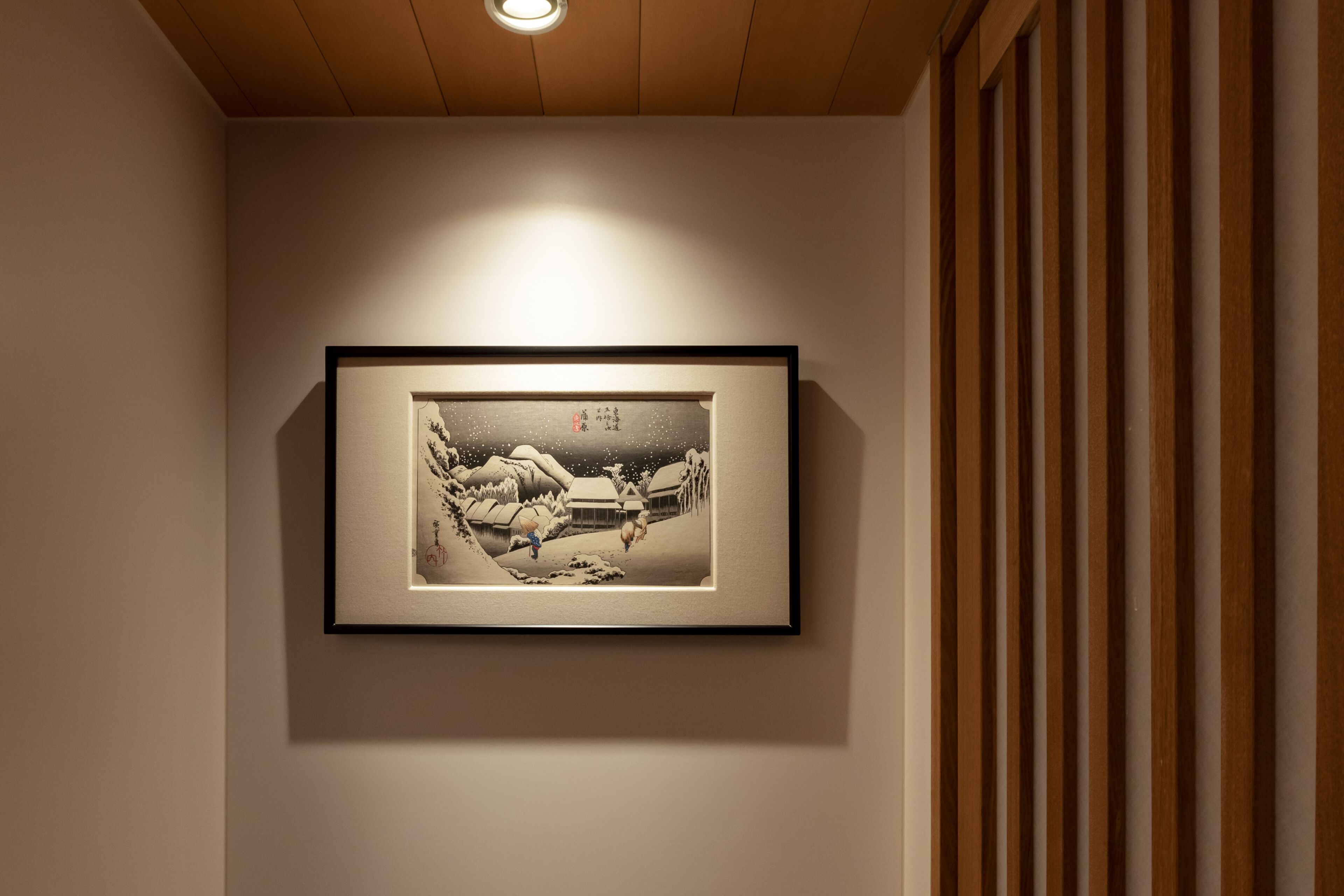 A framed artwork on a wall in a room with wooden paneling and a ceiling light.