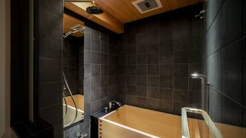 Un baño moderno con una bañera de madera, cabina de ducha de vidrio y paredes de azulejos oscuros.