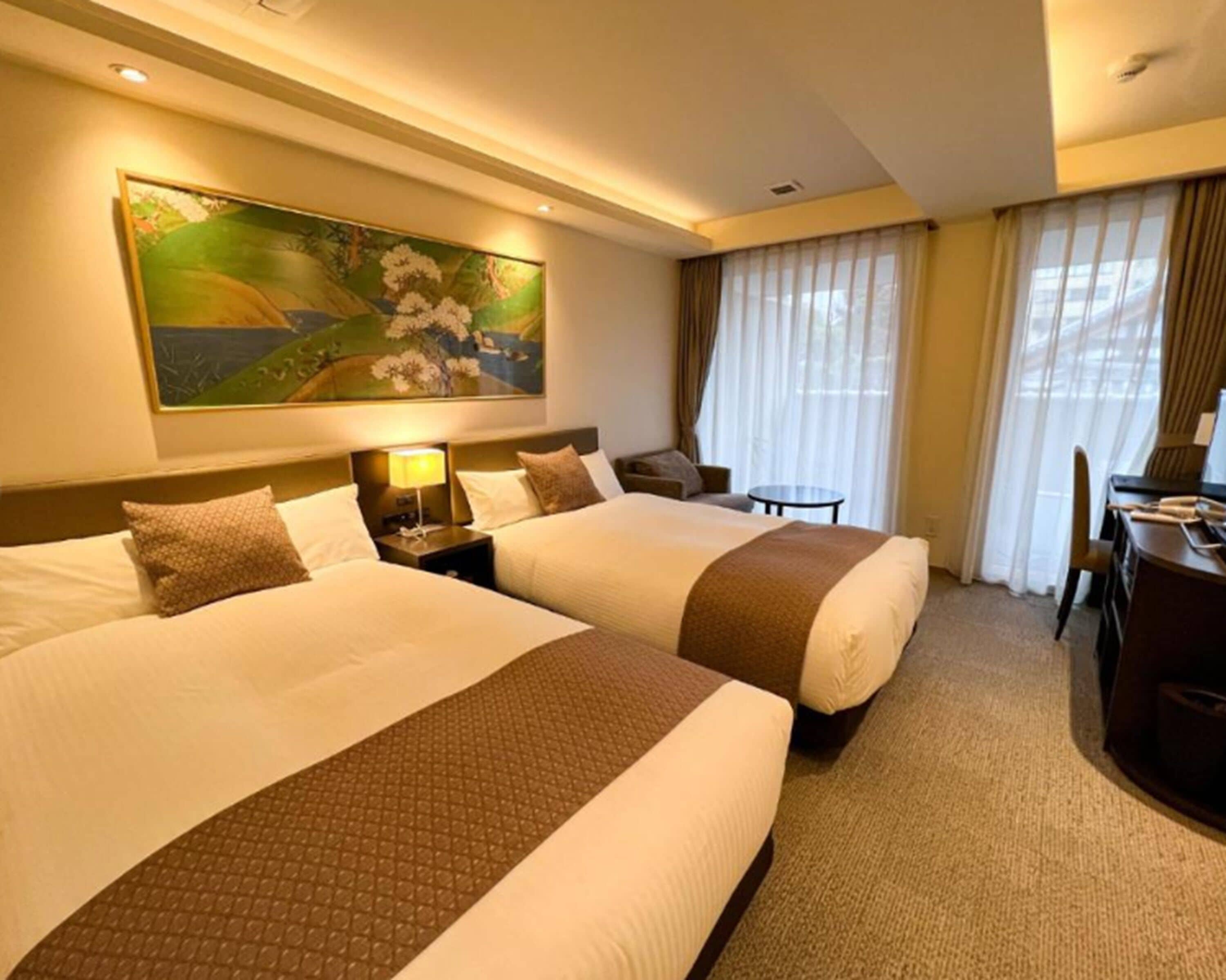 A hotel room with two beds, a desk, a chair, a small table, and a painting on the wall.