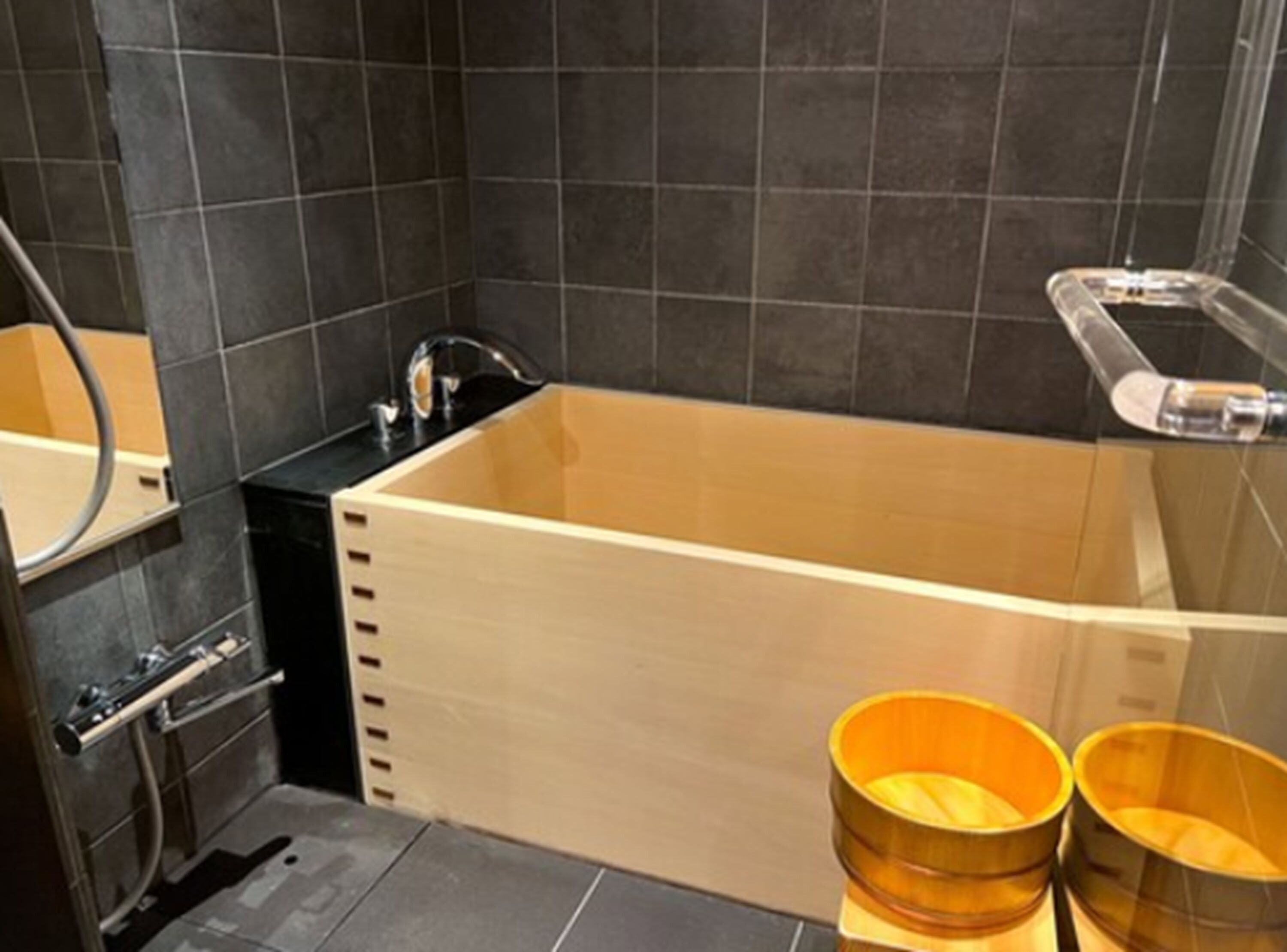 Un baño moderno con una bañera de madera, un lavabo negro y dos cuencos de madera.
