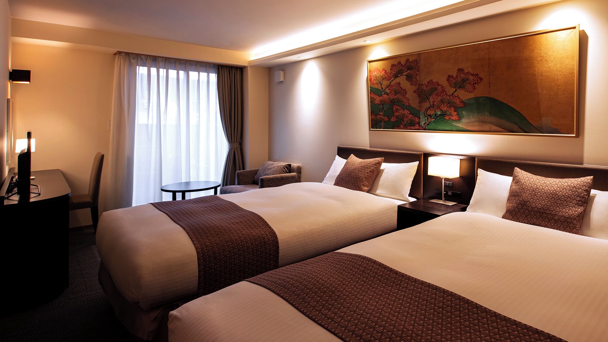Quarto de hotel com duas camas, uma escrivaninha, uma cadeira, uma mesinha e um quadro na parede.