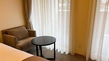 A hotel room with a bed, a sofa, a small round table, and a window with sheer curtains.
